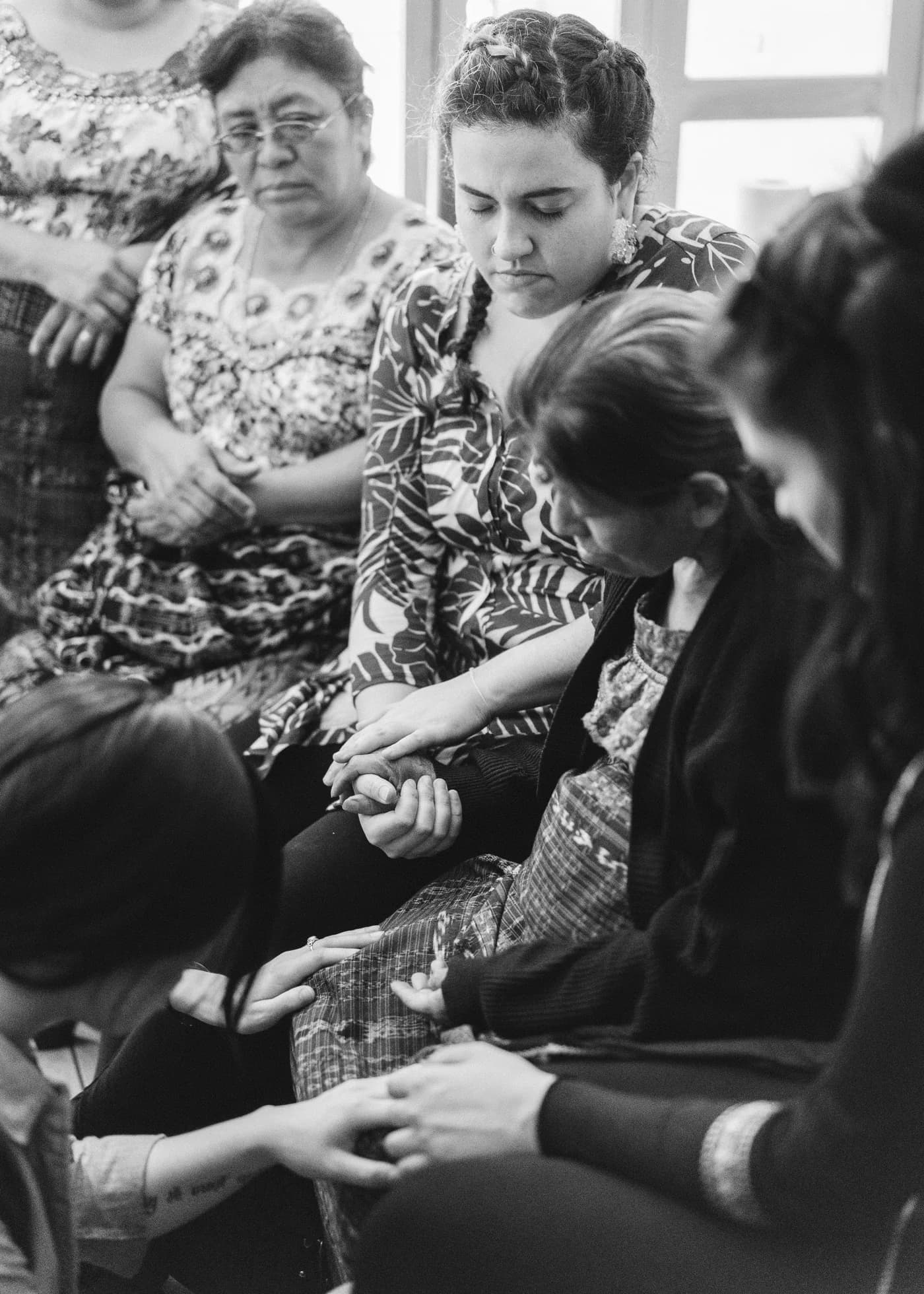 Two women's hands held together in a lap during a session, one pair older and weathered, the other younger, photographed in black and white.